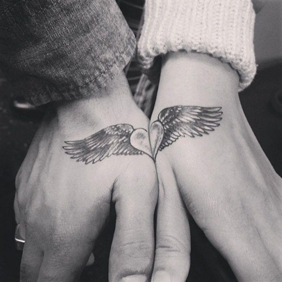 Zwei Hände mit einem gemeinsamen Flügel-Tattoo, dessen Spitzen ein Herz bilden.